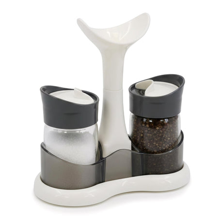 Three spice shakers containing salt and pepper flank a central white ceramic dipping vessel on a tray.
