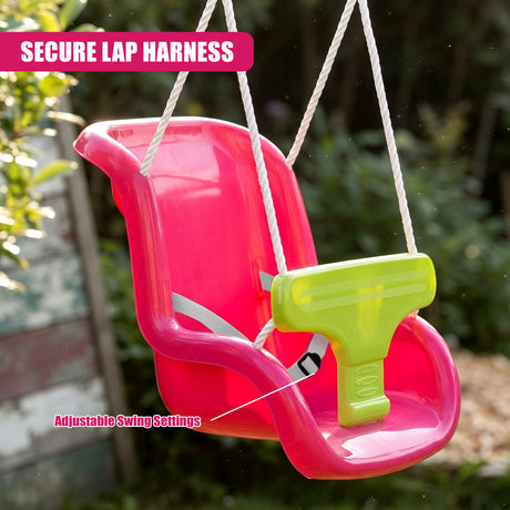A pink toddler swing seat with a lime green harness and white ropes, suspended outdoors against a blurred garden background