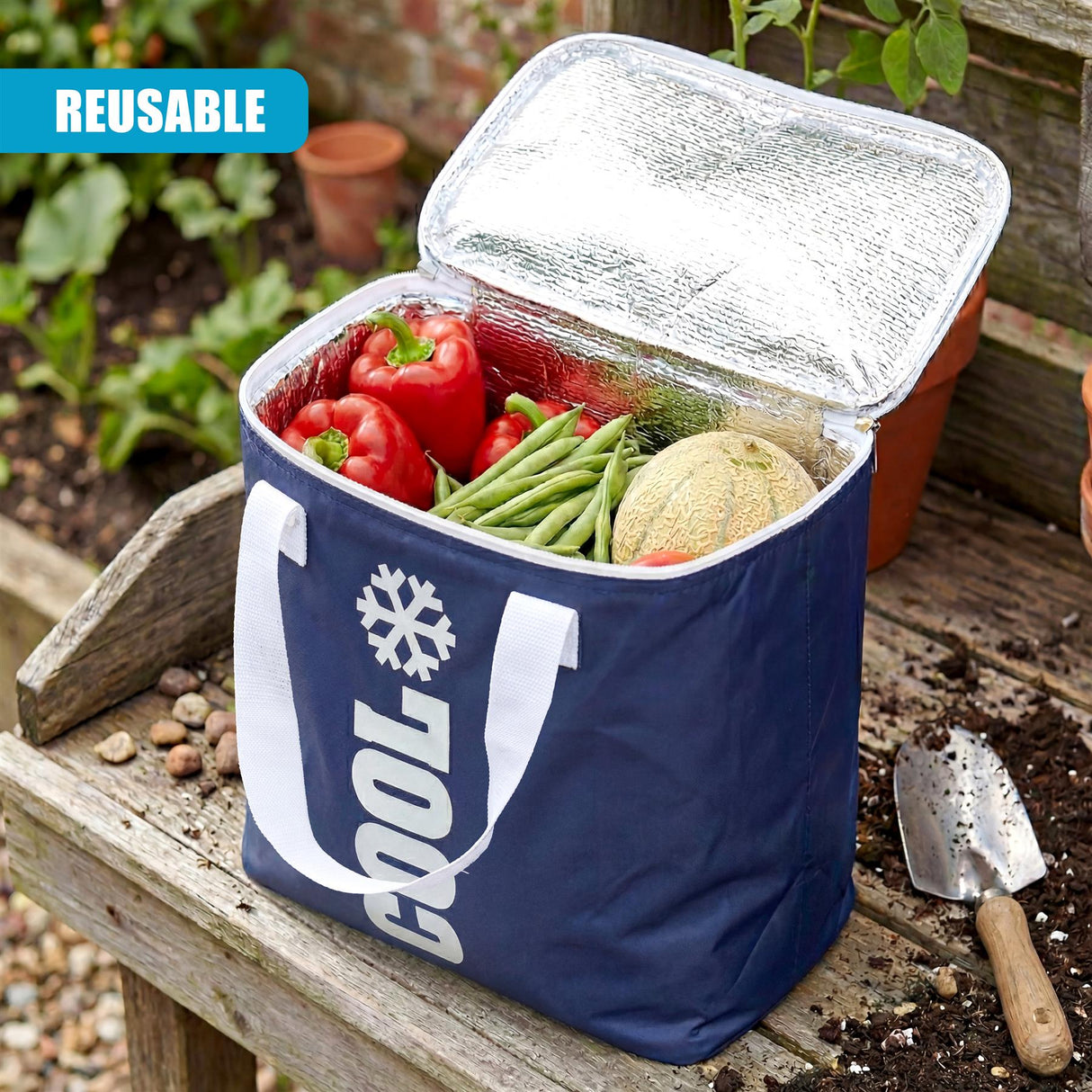 Open blue cooler bag containing colorful vegetables on a wooden surface beside a gardening trowel.