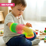 A child sits on the floor, playing with a colorful, flexible, and fun Slinky-like toy. The toy is made of multiple interconnected rings, each in a different color, and is being used as a makeshift arm band, with the child's arm wrapped in the colorful rings. The child is focused on the toy, playing with it, and the background is blurry, with toys and blocks scattered around. - UKBuyZone