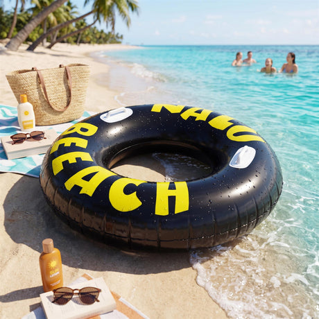 Black inflatable ring with yellow lettering rests on wet beach sand near the ocean.