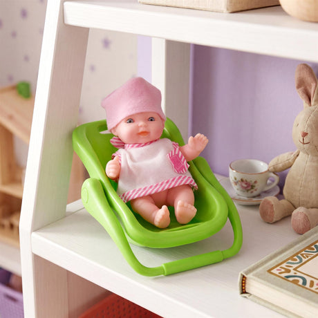 Doll in a green rocker, sitting on a shelf with a stuffed rabbit, teacup, and books.