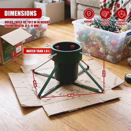 A green metal Christmas tree stand with a water tank, shown on cardboard surrounded by storage boxes and decorations