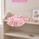Pink knitted doll outfit featuring white trim, cat embroidery, and matching baby booties.