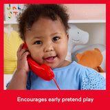 A young child smiles while holding a bright red toy telephone against their cheek.