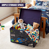 The Magic Toy Shop Blast Off Large Storage Box filled with toys and books, sitting on a carpeted floor next to a bed