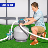 Man interacts with a large grey water filtration unit, connecting white hoses on green grass.