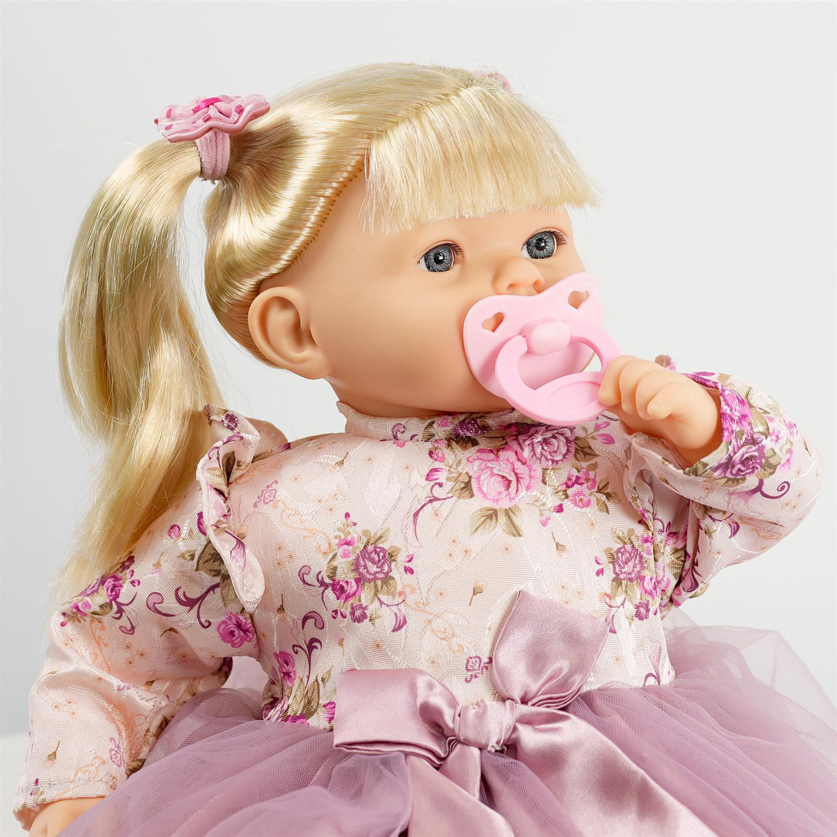 This is a doll from the 'ukbuyzone' with long hair, wearing a floral dress, and holding a pacifier in its mouth. It is approximately 18 inches tall.