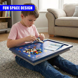 A boy plays with colorful game pieces on a blue activity lap tray while seated on a rug.