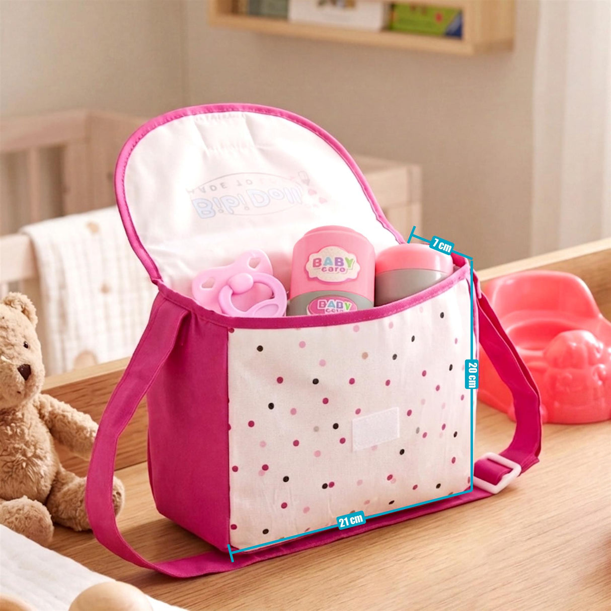 Spotted pink changing bag displays a set of miniature baby accessories and toys.