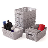 Multiple gray lattice storage baskets arranged with rolled linens, bottles, and a red container.