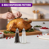 Two clear glass salt and pepper shakers stand on a countertop near a roasted whole chicken.