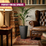 Tall, dark gray, ribbed flower pot holding lush green tropical foliage near a leather armchair.