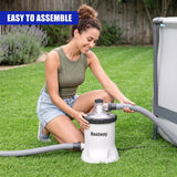 White circular pool filter pump unit with attached hoses resting on green grass.