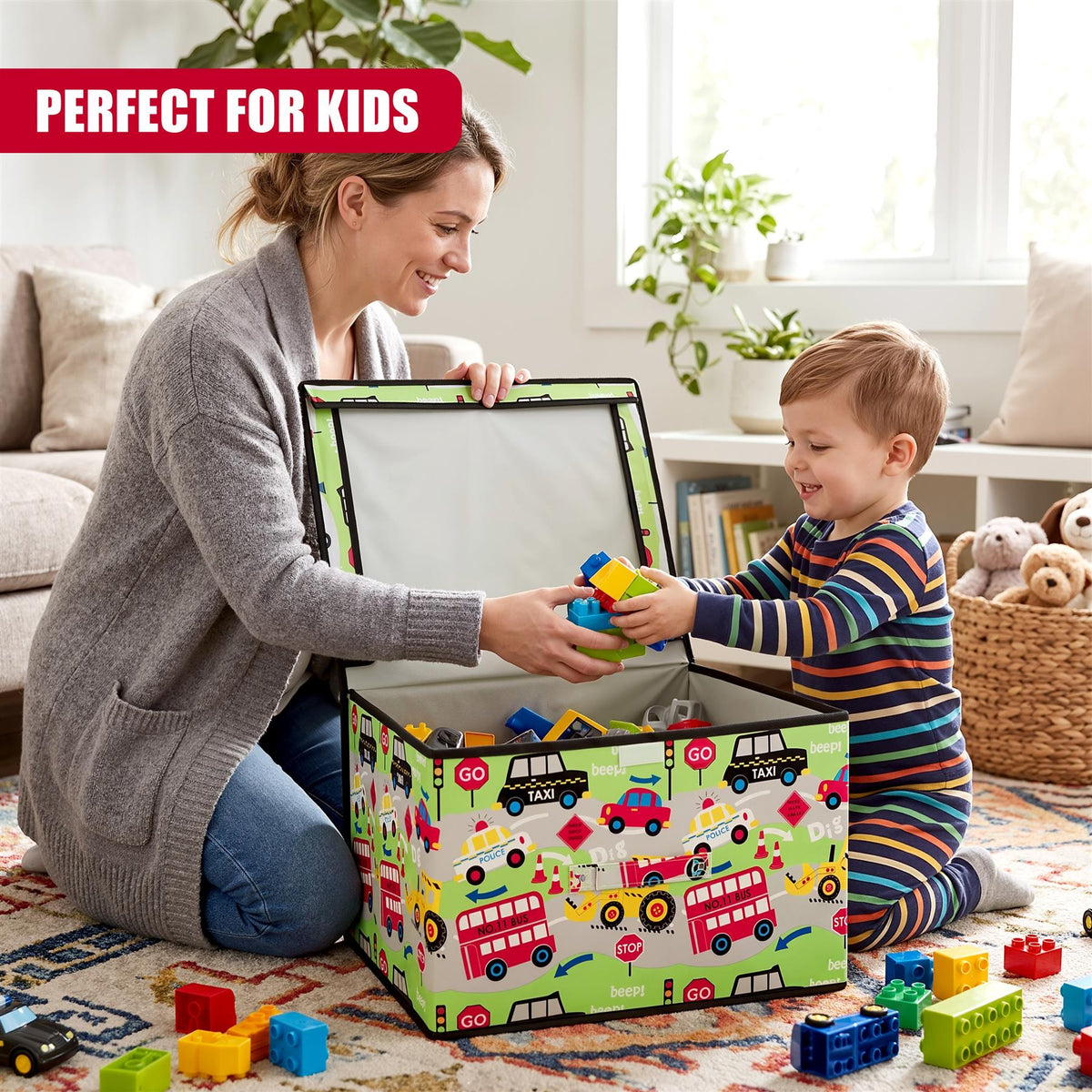 A smiling woman and young boy play together on a rug, passing colourful building blocks into a large Road Works storage box