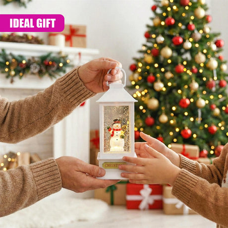 Hands holding a lighted Christmas lantern featuring a snowman figure against a decorated Christmas tree.