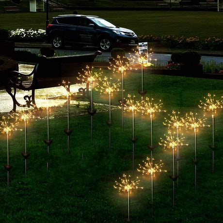 This is an image of a solar-powered starburst stake light set up on a lawn at dusk. The lights are in the shape of stars and are turned on. There are also several other decorative lights placed in front of the starburst lights.