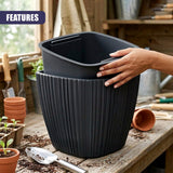 A hand inserts a black container into a larger, ribbed black planter pot on a wooden surface.
