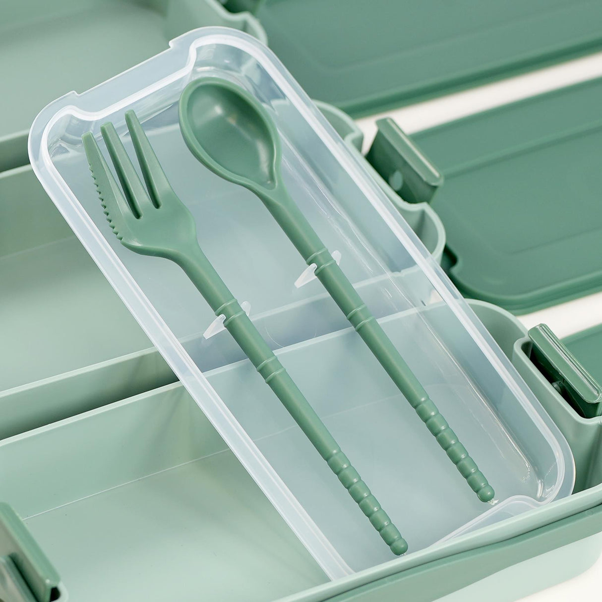 A plastic case containing two green spoons in a compartment.