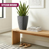 Gray, cylindrical flower pot holding a green plant sits on a wooden table with stacked books and sandals.