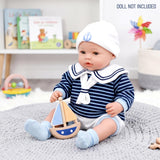 A doll dressed in a navy striped sailor outfit sits next to a wooden sailboat toy.