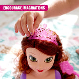 Hand placing a glittery pink tiara accessory onto the doll's reddish-brown hair.