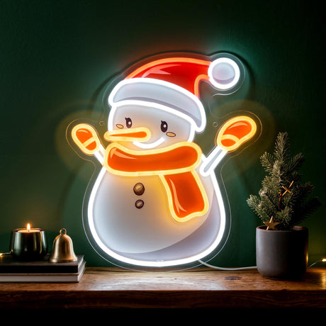 A GEEZY Christmas neon light shaped like a snowman wearing a red hat and orange scarf, displayed on a wooden shelf next to a