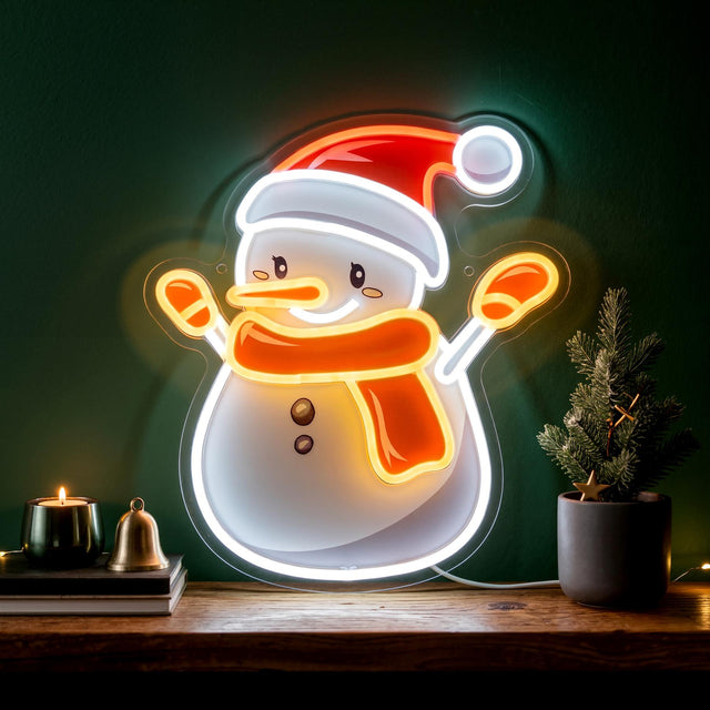 A GEEZY Christmas neon light shaped like a snowman wearing a red hat and orange scarf, displayed on a wooden shelf next to a