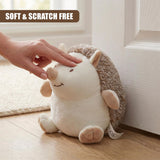 Hand petting a plush hedgehog door stop resting against white wood trim.