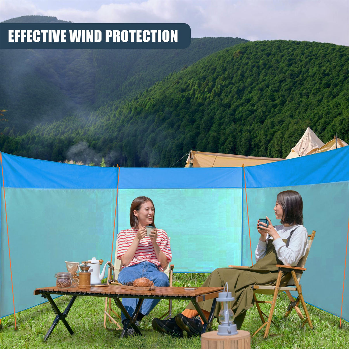 Two women seated at a wooden table under a blue canopy in an outdoor setting.