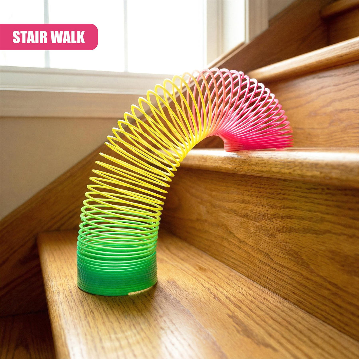 A colorful, spiral-shaped toy with a green, yellow, and pink gradient, resembling a Slinky, sitting on a wooden staircase, with a window in the background. - UKBuyZone