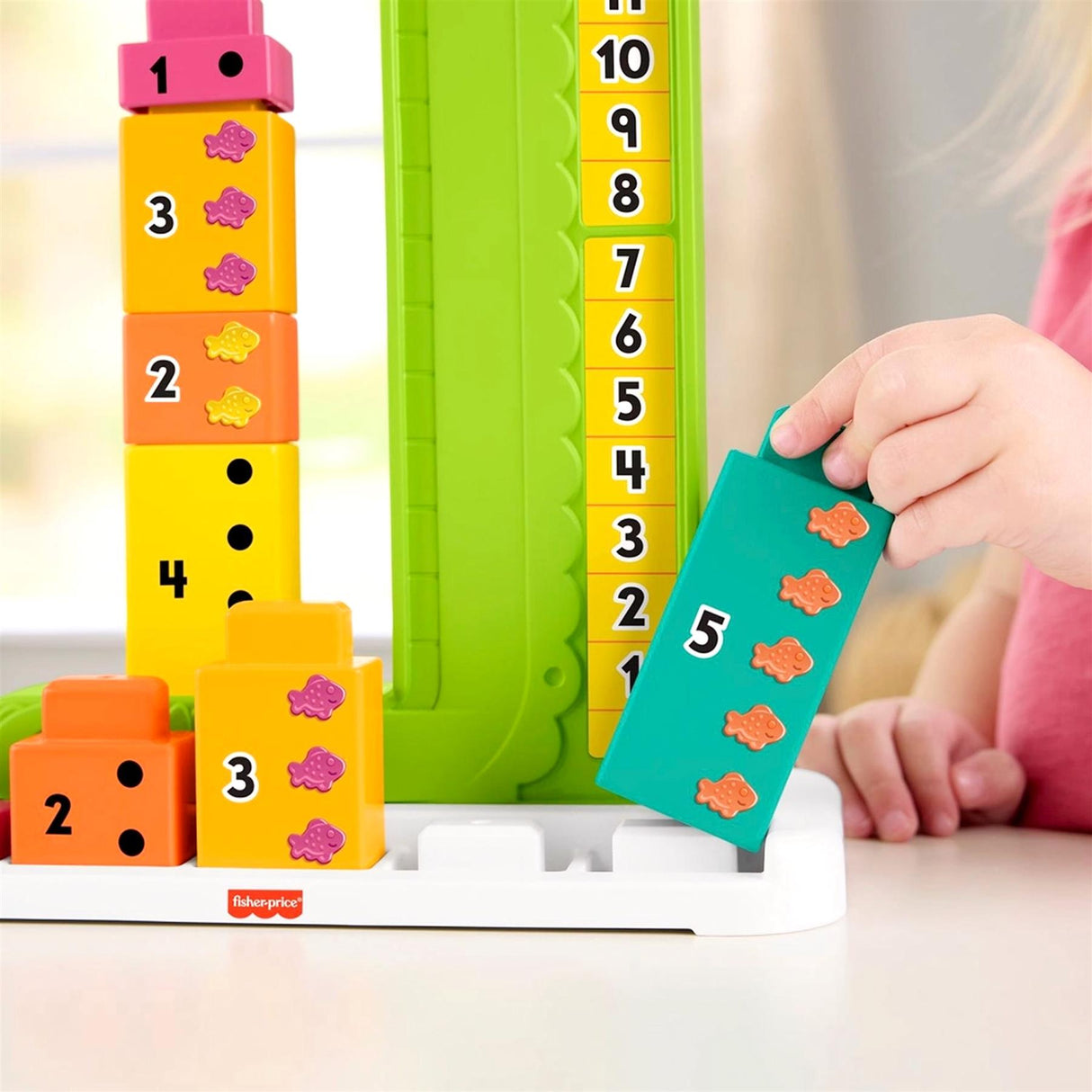 Stacked counting blocks, a green number board, and a teal alligator toy piece are displayed on a tray.