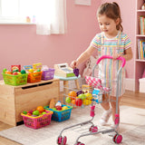 A young girl pushes a metal shopping cart filled with plastic play food and various colorful toys.