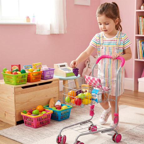 A young girl pushes a metal shopping cart filled with plastic play food and various colorful toys.