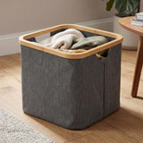 Gray fabric laundry hamper with a visible wooden rim, filled with folded white clothes.