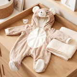 Beige bear onesie with hood and ears, displayed next to folded cream-colored garments on a wooden surface.