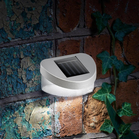 Gray solar light fixture attached to a rough brick wall next to green ivy leaves.
