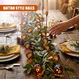 Solar string lights with rattan bulbs illuminate a wooden table setting with foliage and dishes.