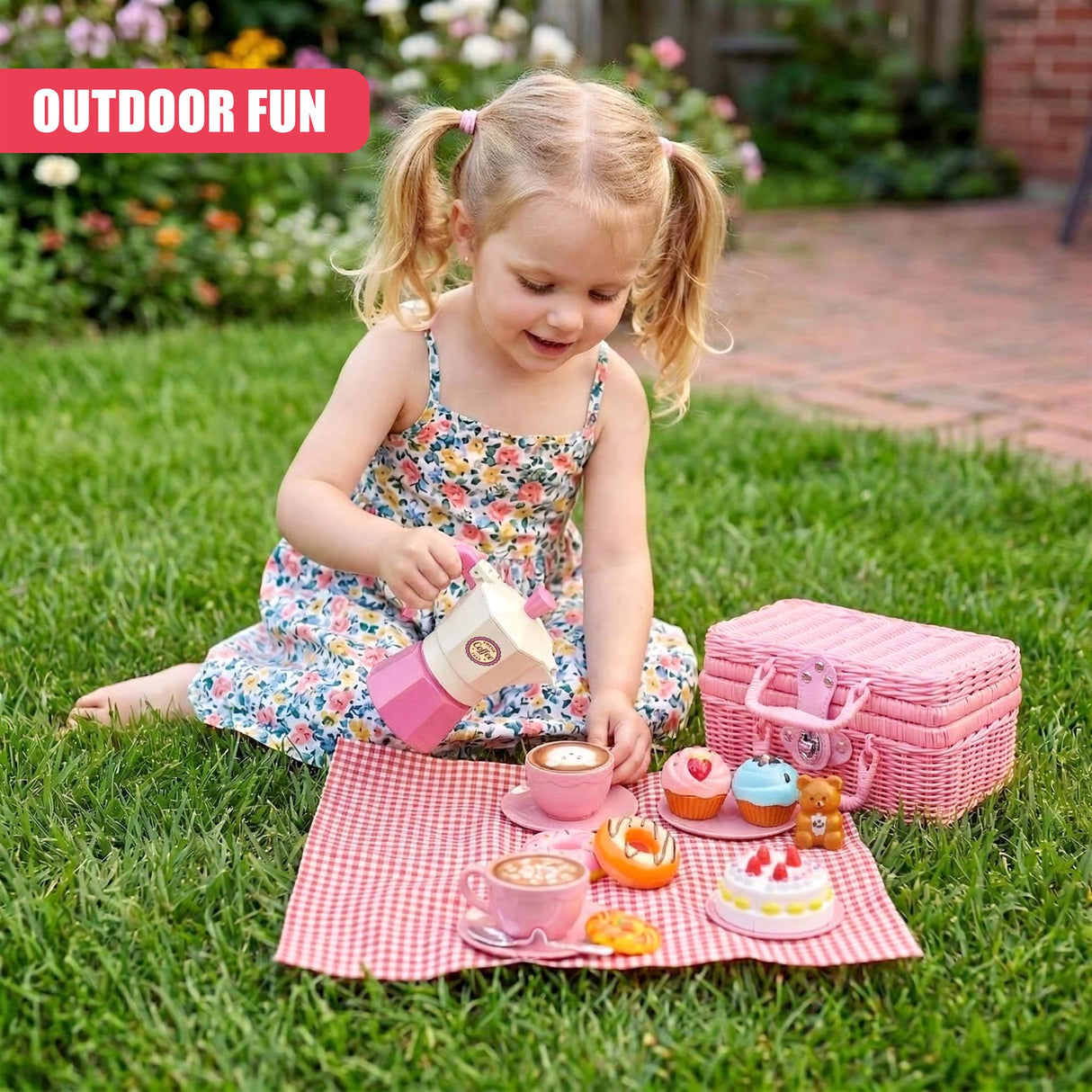 Girl playing with a colorful tea party set and a pink woven picnic basket laid out on the grass.