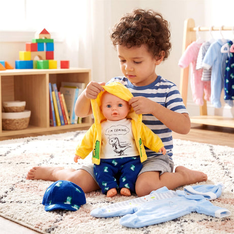 A boy plays with a doll wearing a yellow shirt, surrounded by blue clothing accessories and pants.