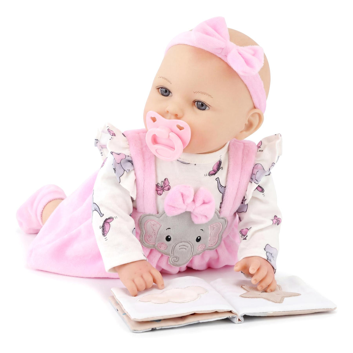 Large baby doll with pink clothes and pacifier sitting beside an open book with drawings.