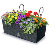 Black rectangular planter box filled with colorful flowers, greenery, and two curved hangers.