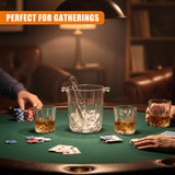 Whiskey glasses and an ice bucket rest on a green table surrounded by playing cards and poker chips.