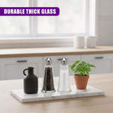 A set of three glass salt and pepper shakers displayed on a marble tray with a small potted plant.