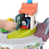 Colorful toy train set featuring a green track, blue train, orange station, and pink play area.