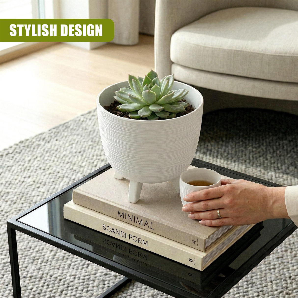 White flower pot with legs holding a succulent, set on a stack of books on a glass table.