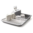A modern gray dish drying rack holding two mugs, two forks, and several drinking glasses.