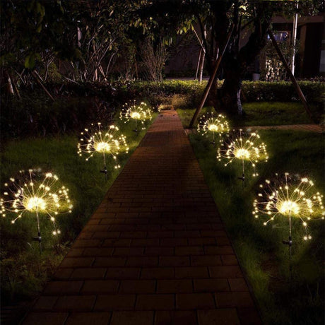 A set of nine solar powered fairy lights in two stakes on a brick pathway at night.