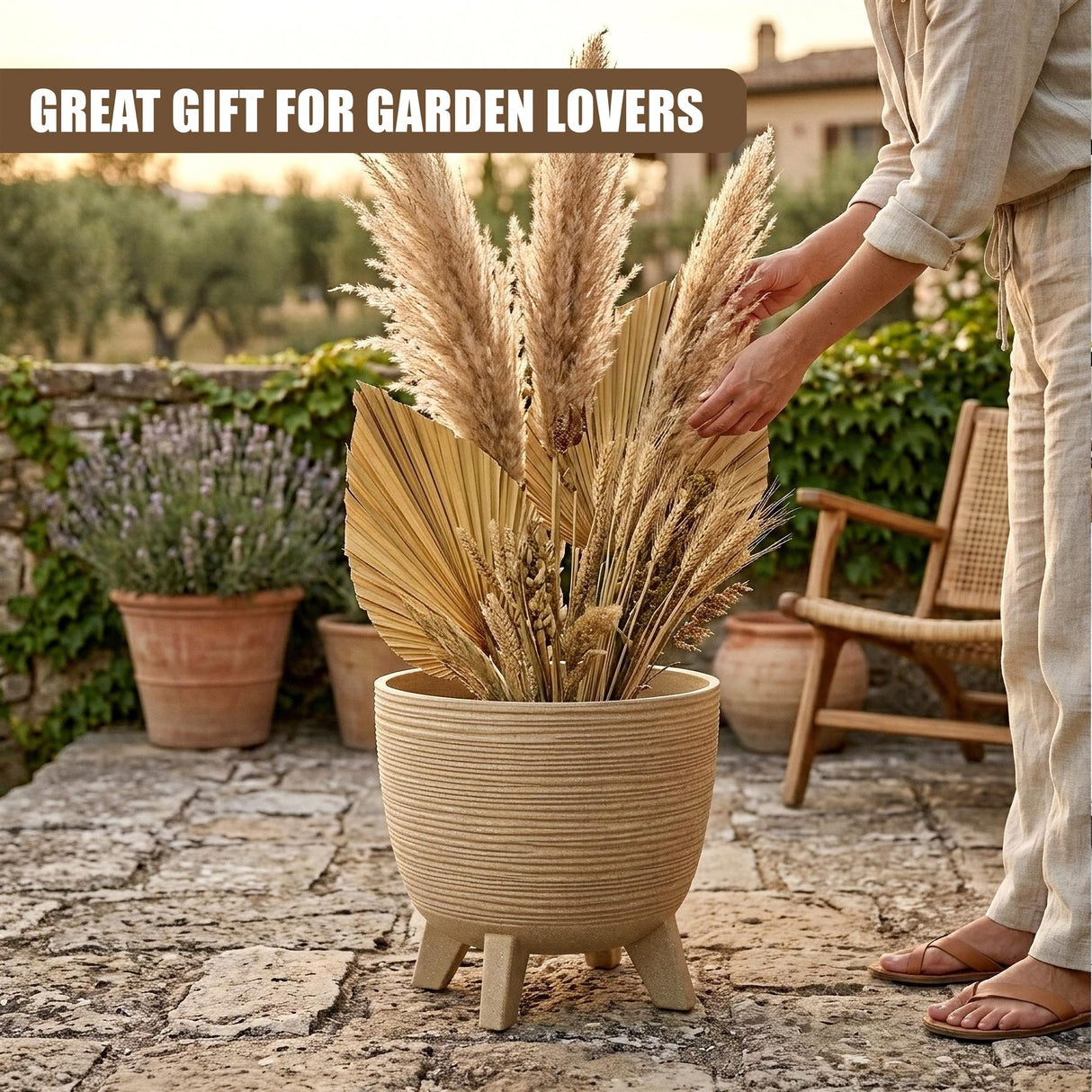 Beige pot with three legs filled with tall, dried decorative grasses and assorted foliage.