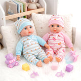 Two doll twins sit with shoes, cubes, plush toy, and various pastel accessories on white fur.